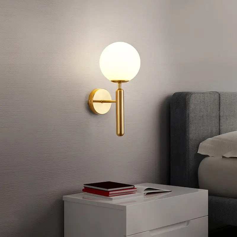 single head glass wall sconce with warm white LED light and gold metal finish mounted in bedroom setting
