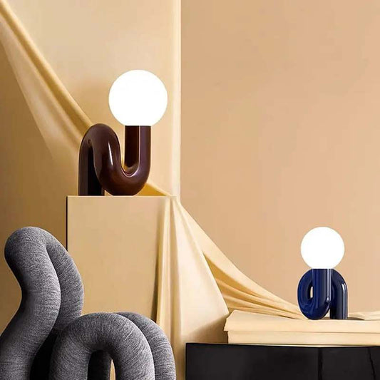 Modern LED table lamp with round white bulb and curved resin base in burgundy and blue colors for elegant interiors