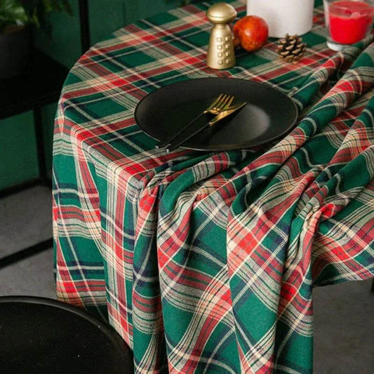 Green Christmas Tablecloth with red white green plaid pattern on round table with black plates and utensils in festive setting