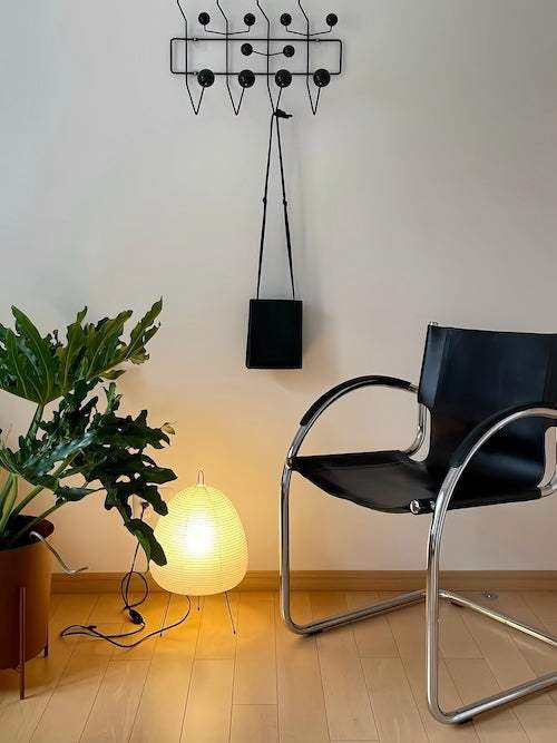 glowing rice paper lamp beside black chair and green plant in modern interior