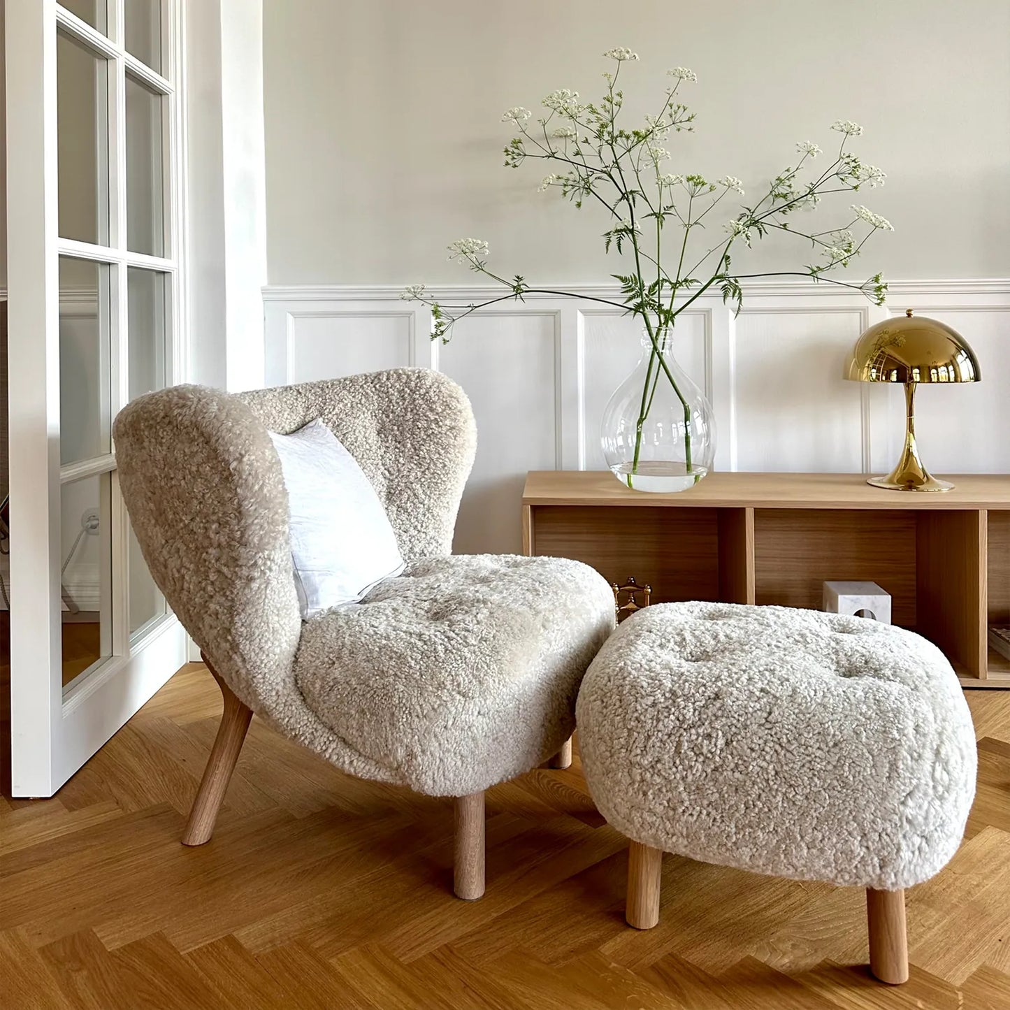 Little Petra Lounge Chair and Ottoman in cozy faux sheepskin with solid wood legs, showcasing retro Danish design in a modern living space.