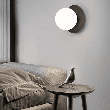 Modern round wall sconce with frosted glass globe and black metal base illuminating bedroom with warm white light