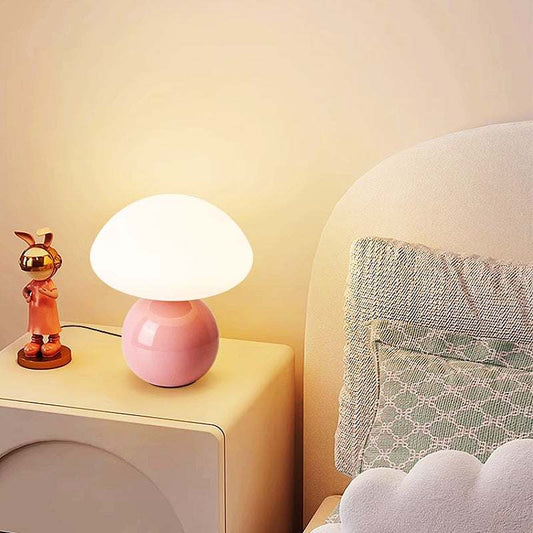 Pink ceramic table lamp with mushroom-shaped white lampshade on bedroom nightstand providing cozy ambient light