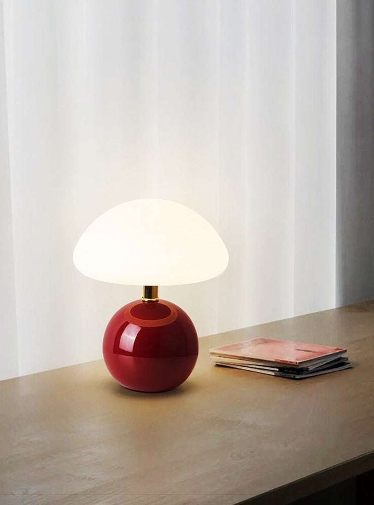 Red ceramic table lamp with white mushroom-shaped lampshade on wooden surface for cozy ambiance