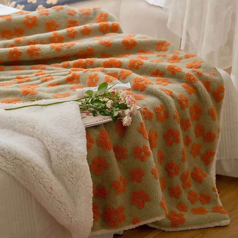 full fleece blanket with orange floral pattern and soft white fleece backing draped on bed with flowers