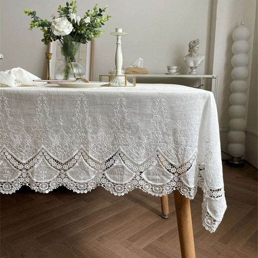 Handmade white cotton tablecloth with embroidered patterns and scalloped edges on wooden table