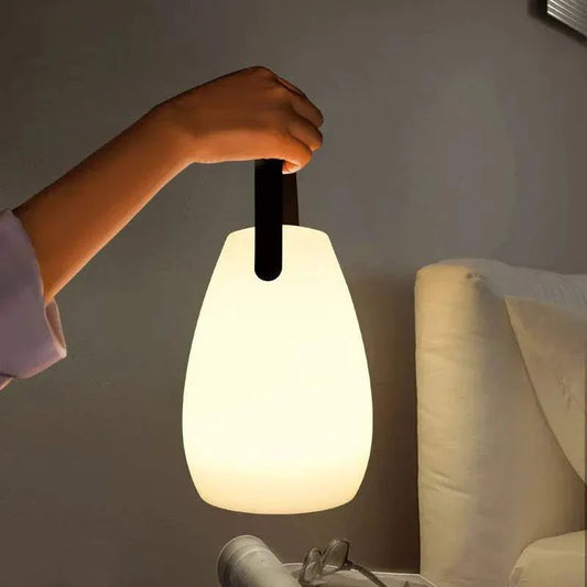 Hand holding glowing portable lamp with black handle near couch in dim room