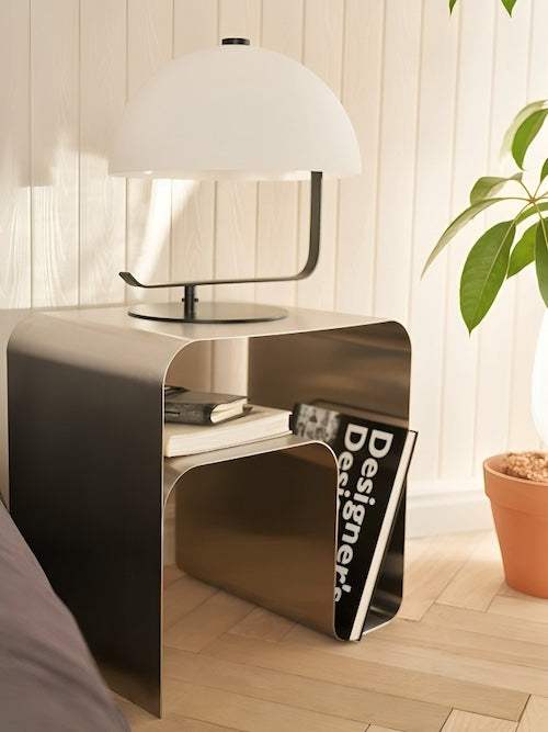 Minimalist stainless steel metal side table with smooth surface and modern design next to potted plant and lamp