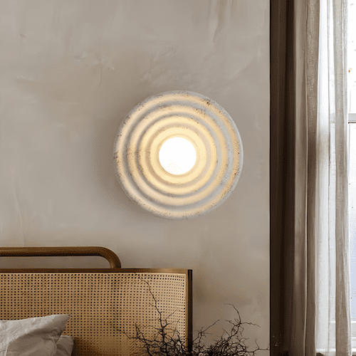 Modern round wall light fixture with frosted glass and concentric design, mounted above bed in cozy room