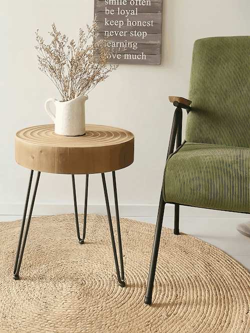 Minimalist round side table with wooden top and metal legs beside green chair on woven rug