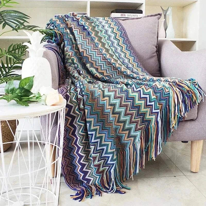 Boho corner sofa cover with colorful zigzag plaid pattern and fringed edges draped over a grey sofa