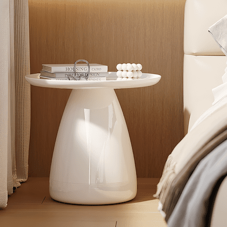 White round PVC small side table next to bed with books and decor on top