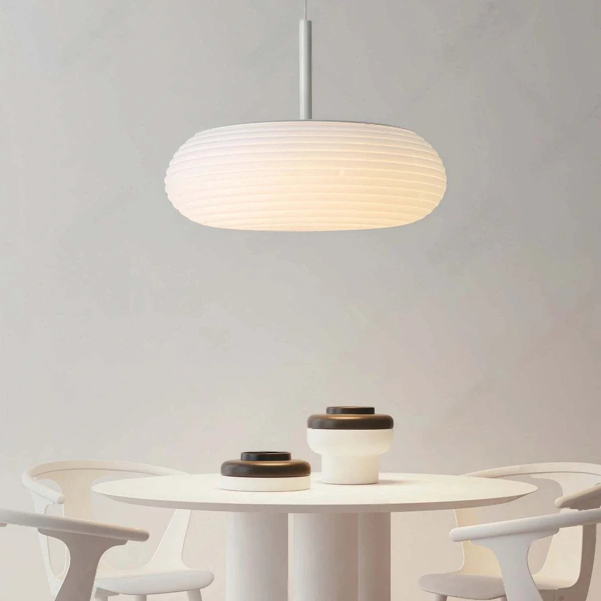 Minimalist pendant light with flattened oval ribbed lampshade hanging over dining table in modern Nordic interior