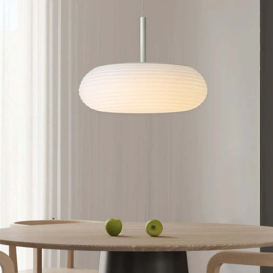 Minimalist Nordic pendant light with flat oval ribbed shade hanging over wooden dining table