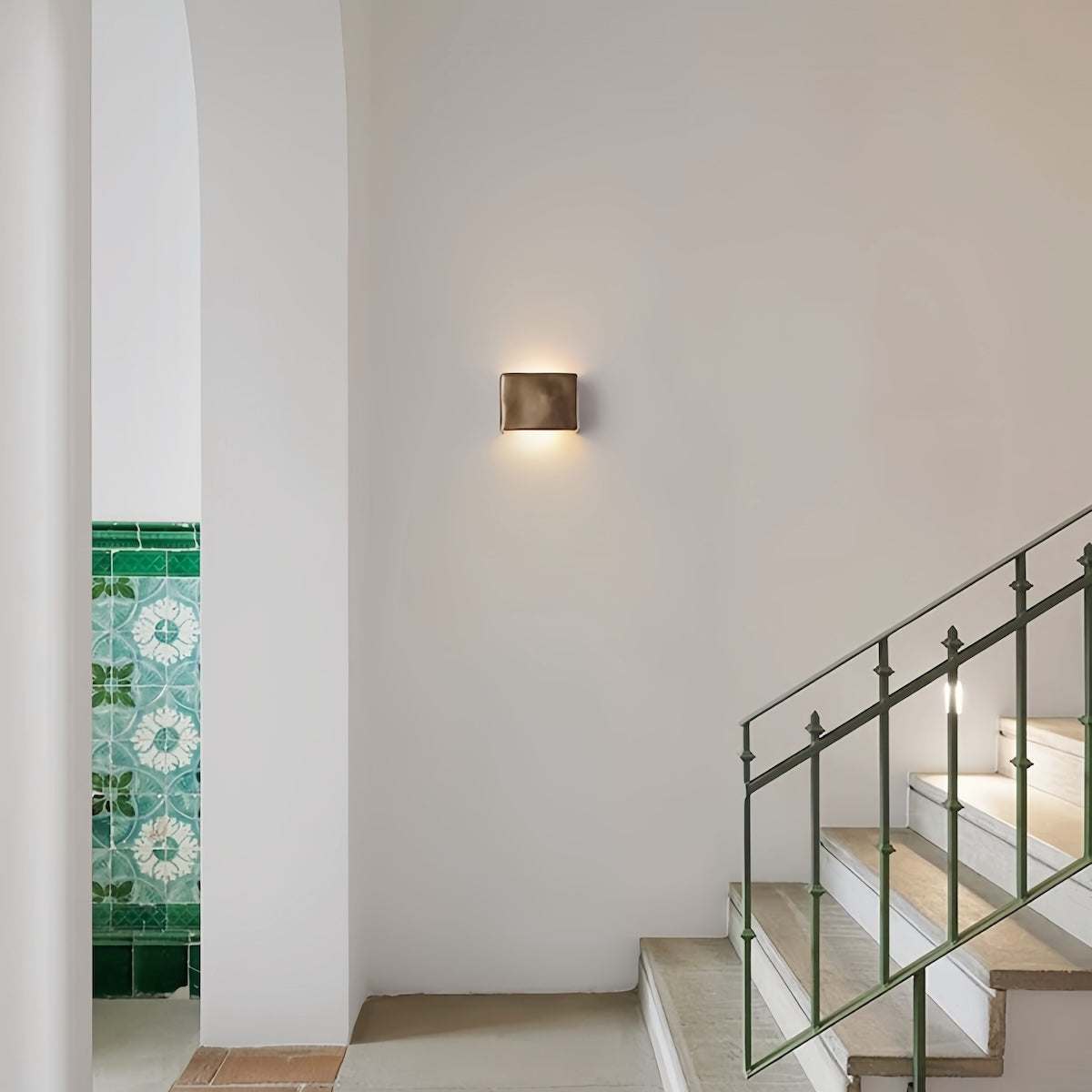 Scape Wall Light mounted on white staircase wall providing soft warm illumination in modern interior with green tiled accent wall.