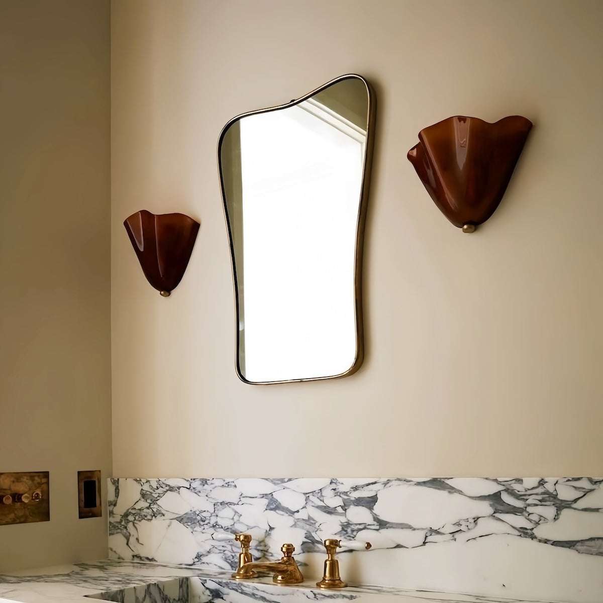 Vintage glass wall lamp with curved brown glass shades on either side of a modern mirror above a marble bathroom sink