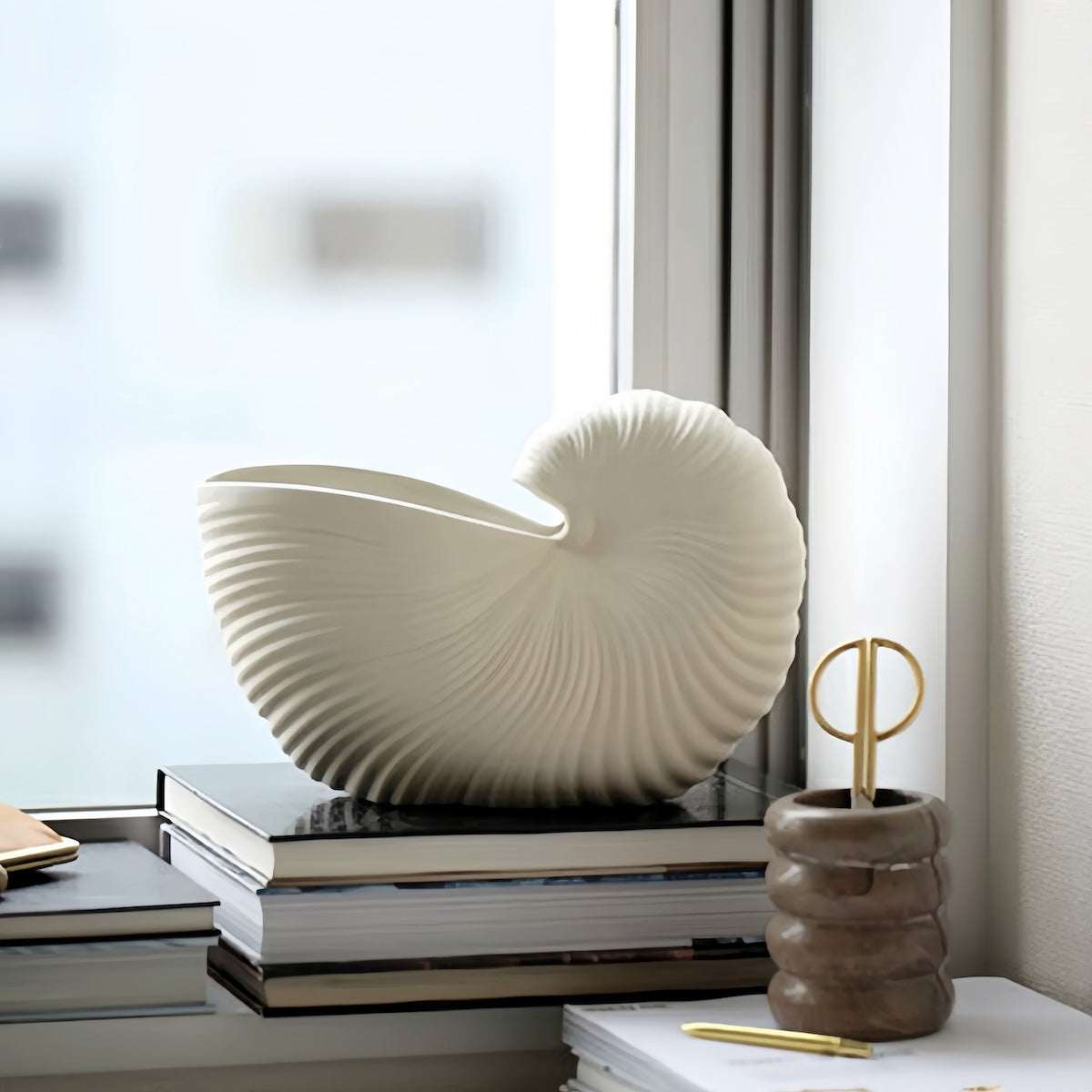 Nordic style ceramic seashell vase on books by window in modern home decor