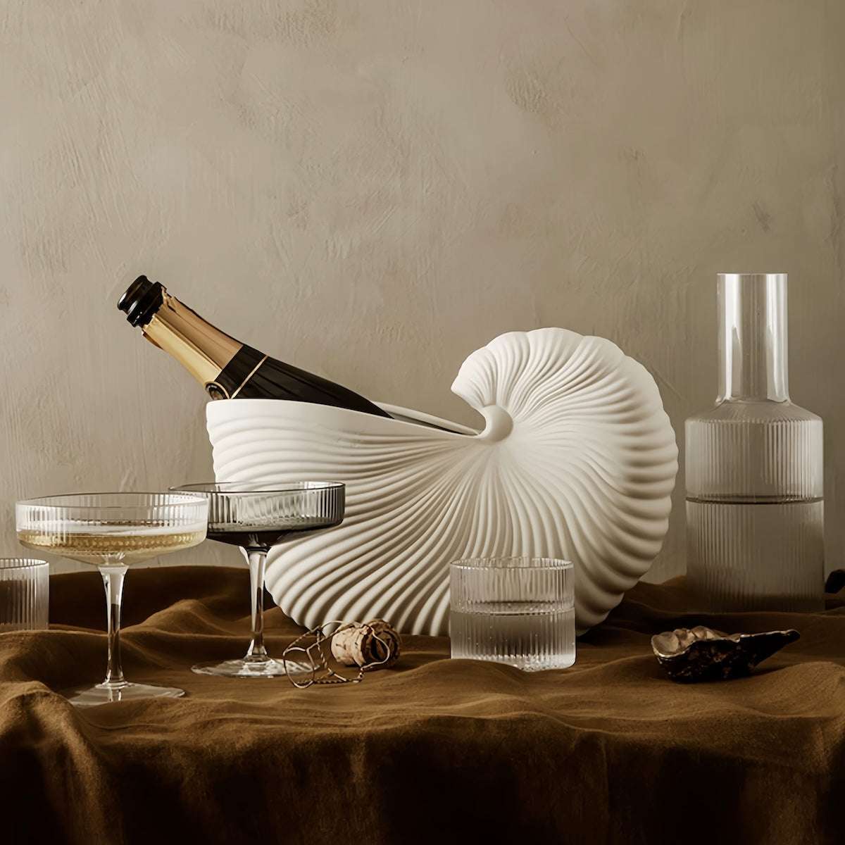 Nordic style ceramic seashell vase with matte finish and nautilus shell design holding a champagne bottle on a brown tablecloth