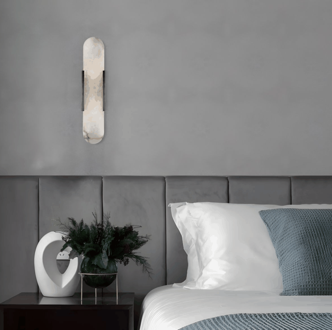 Modern marble wall light with warm gold and black finishes mounted above a gray upholstered bed in a minimalist bedroom setting