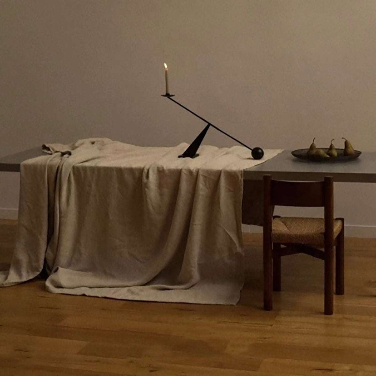 Modern minimalist black candle holder with geometric design on dining table with beige tablecloth and wooden chair