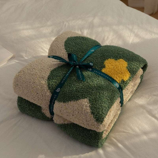 Folded green throw blanket with yellow flower design tied with a green ribbon on white bedding