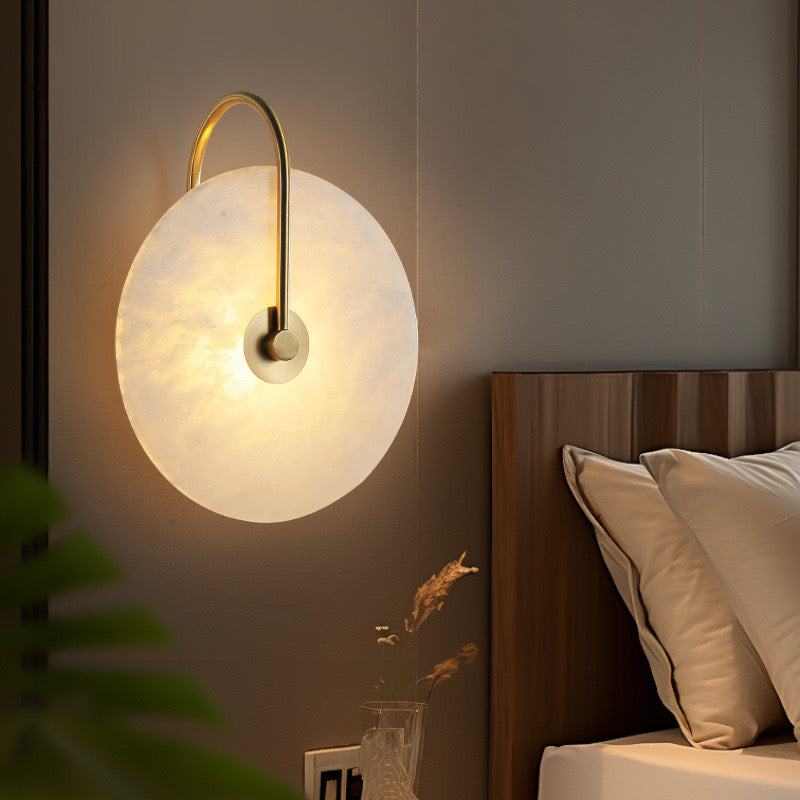 Modern marble sconce wall light with round white marble shade and gold aluminum arm mounted beside bed