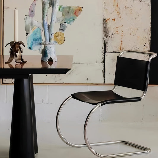Minimalist stainless steel dining chair with sleek design next to modern table, enhancing contemporary dining space.