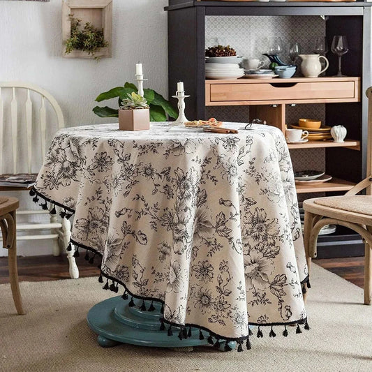 Round tablecloth with black rose floral pattern and tassel trim on round table in cozy dining room setting
