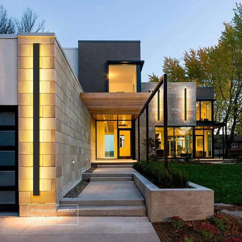 Modern waterproof IP65 outdoor wall light installed on exterior house wall illuminating pathway and garden at dusk