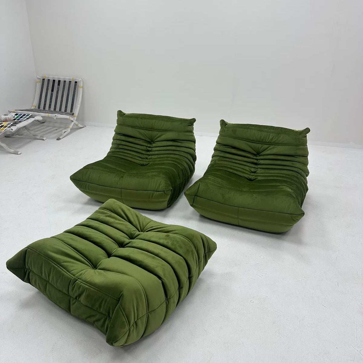Three olive green tufted lounge chairs or floor cushions arranged on a white studio floor against a white wall.