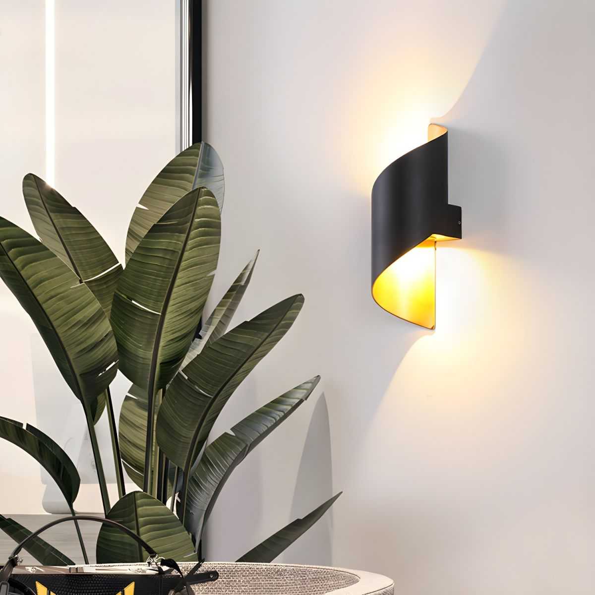 Postmodern unique sconce light with black metal curved design and warm ambient LED lighting mounted on living room wall near green plant