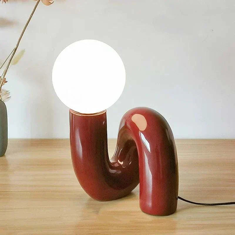 Modern burgundy LED table lamp with curved neotenic design and glowing white bulb on wooden surface